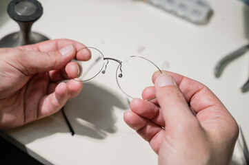 A man repairs a broken eyeglass frame. Close-up of the ophthalmologist's hands