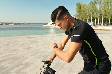 Man checking modern smart watch during training near river