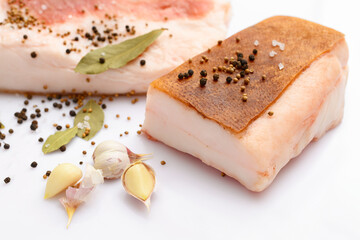 raw lard two pieces and salt, spices and bay leaf on white background, pork fat