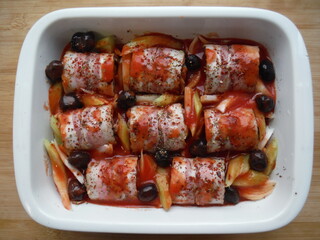meat rolls in bacon with vegetables, olives and spices in a white plate, on a wooden table, the cooking process.