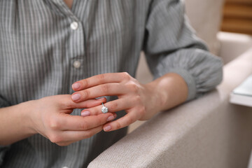 Woman taking off wedding ring indoors, closeup. Divorce concept