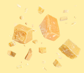 Pieces of delicious parmesan cheese flying on yellow background