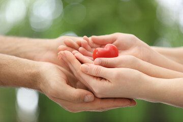 Parents and kid holding red heart in hands outdoors, closeup. Family day