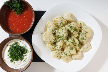 homemade dumplings in the kitchen without decorations. ready-made dumplings on a white plate, served with sour cream and adjika
