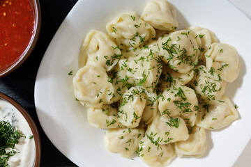 homemade dumplings in the kitchen without decorations. ready-made dumplings on a white plate, served with sour cream and adjika