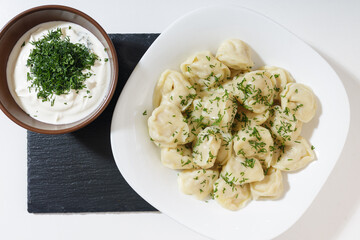 homemade dumplings in the kitchen without decorations. ready-made dumplings on a white plate, served with sour cream