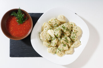 homemade dumplings in the kitchen without decorations. ready-made dumplings on a white plate, served with adjika