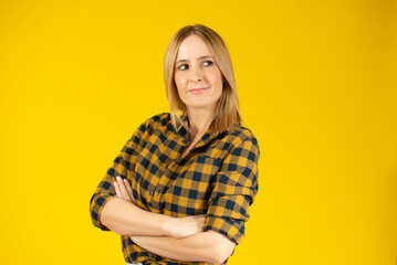 Portrait of a smiling young woman standing with arms folded and looking away at copy space isolated over yellow background