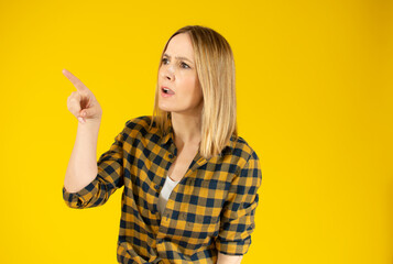 Portrait of beautiful young woman pointing up over yellow background.