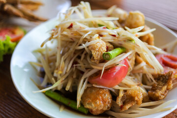Spicy green papaya salad or Som Tum, Thai traditional famous food. Selective focus on middle crispy pork.