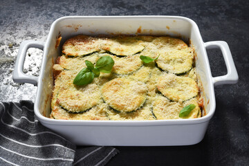 Zucchini gratin with béchamel sauce and parmesan on a dark concrete background. Summer pie with zucchini.