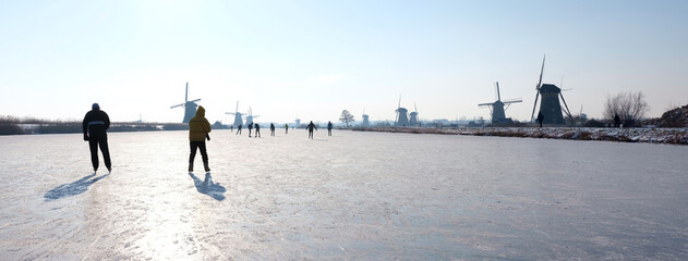 people skate on the ice near kinderdijk with al lot of windmills in holland on sunny winter day - obrazy, fototapety, plakaty