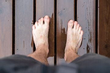 Barefoot male feet stand on a wet wooden floor, after rain, in the open air. 