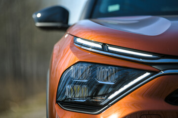 Front headlights and hood of orange modern prestigious car on nature background. Close up.
