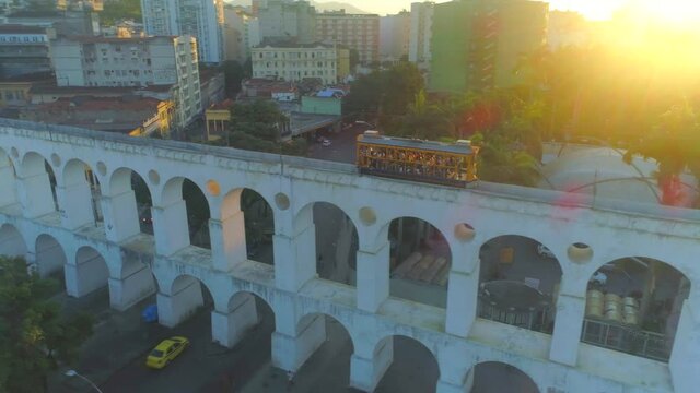 Traditional yellow Santa Teresa tram streetcar passing over the iconic Lapa arches in Rio de Janeiro at sunset