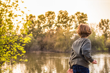 Naklejka na ściany i meble Child Throwing Stones Into The River. Boy Playing By The River At Sunset. Lifestyle And Nature