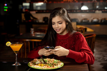 Portrait of a pretty young girl checking her phone while having lunch at the restaurant.