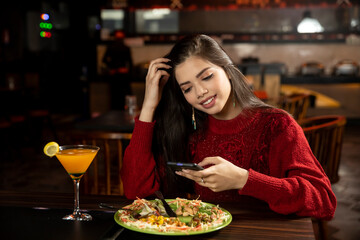 Portrait of a pretty young girl checking her phone while having lunch at the restaurant.
