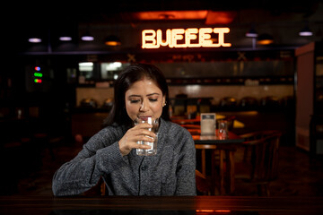 Portrait of a woman drinking water in a restaurant.