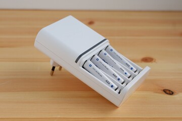 Rechargeable AAA battery in a white charger on wooden background.
