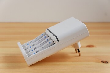 Rechargeable AAA battery in a white charger on wooden background.