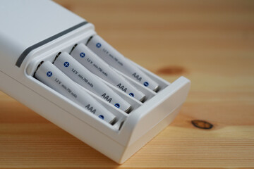 Selective focus rechargeable AAA battery in a white charger on wooden background.