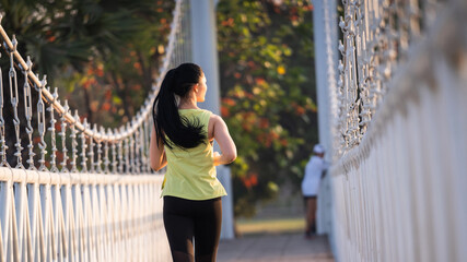 A young Asian woman athlete runner jogging in city stadium in the sunny morning to keep fitness and healthy lifestyle. Active healthy runner jogging outdoor. Sports and recreation