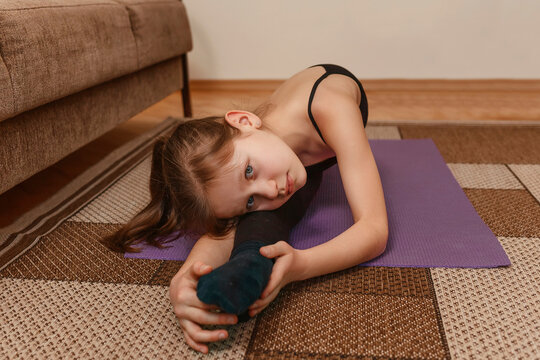 Little girl doing stretching at home. The child sits in a twine on the floor