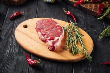Side view on raw piece of meat with rosemary on the wooden board