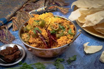 Indian rice and okra pilaf served in a copper finish bowl on blue table