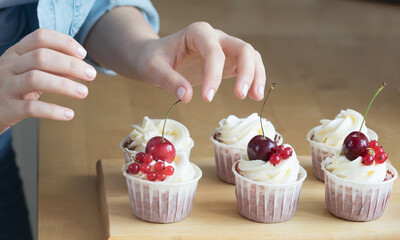 Lifestyle, hobby and people concept. Hands close-up of young woman pastry chef decorates cupcakes with berries