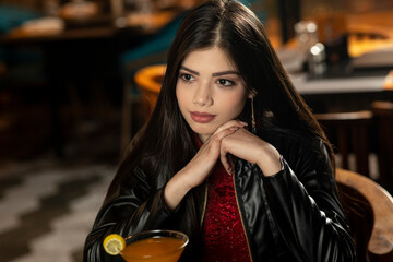 A pretty young female looking away from the camera while drinking juice sitting in a restaurant.