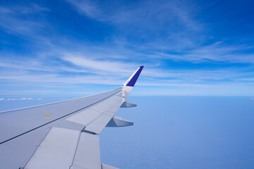 Photo of airplane wing with clouds background, horizon line and clear blue sky
