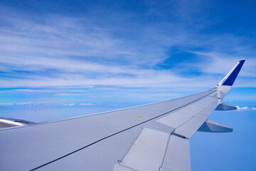 Photo of airplane wing with clouds background, horizon line and clear blue sky