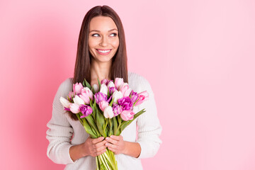 Photo of dreamy happy nice young woman look empty space hold flowers smile isolated on pastel pink color background