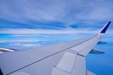 Fototapeta premium Photo of airplane wing with clouds background, horizon line and clear blue sky