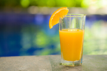 holidays and relax conceptual image of fresh orange juice by swimming pool side at tropical garden