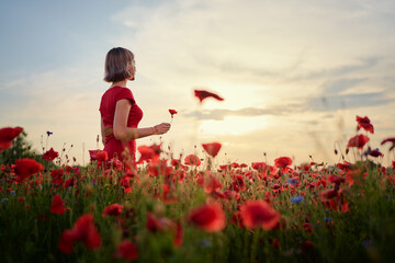Summertime. Young woman in dress walking on red poppy field.