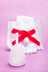 Eco-friendly siliconemenstrual cup with pad and tampon on pink background.