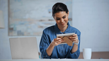 pleased woman holding photo frame near laptop on desk