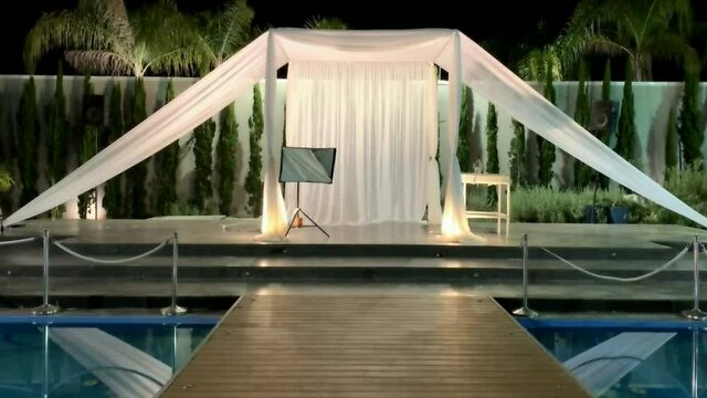 Jewish traditions wedding outdoor ceremony. Wedding canopy (chuppah, hupa) made of white fabric against the background of evening sky, palms and an artificial reservoir decorated with balloons. HD