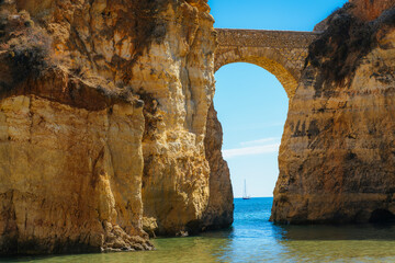 Detailed View of arched bridge with sailboat in Students Beach in Lagos, Algarve, Portugal