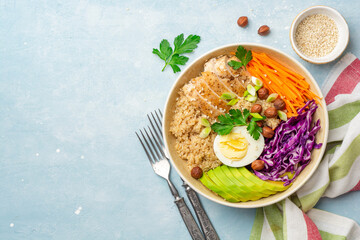 Healthy buddha bowl with quinoa, chicken, egg, avocado, carrot, red cabbage, hazelnuts and greens on blue concrete background