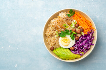 Healthy buddha bowl with quinoa, chicken, egg, avocado, carrot, red cabbage, hazelnuts and greens on blue concrete background