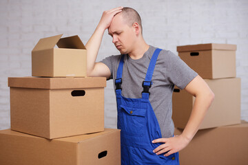 hard work and stress concept - tired loader or deliveryman between big boxes