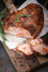 Large sliced piece of baked pork back with seasonings and dried apricots on a wooden kitchen board
