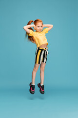 Jumping high. Happy, smiley little caucasian girl isolated on blue studio background with copyspace...
