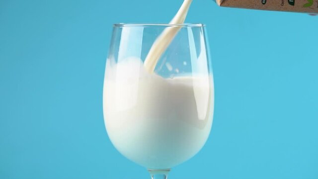 A hand pours milk into a glass on a blue background. Slow motion
