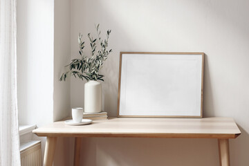 Home office concept. Empty horizontal wooden picture frame mockup. Cup of coffee on wooden table....