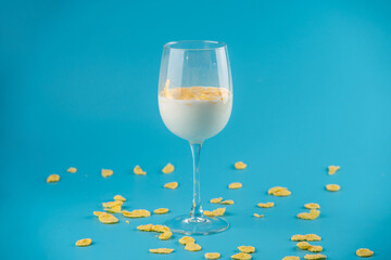Milk in a glass and scattered yellow corn flakes on a blue background